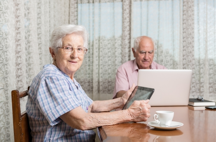 Een afbeelding met hierop twee oudere mensen achter een laptop en tablet